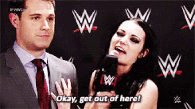 a man in a suit and tie stands next to a woman holding a microphone and saying okay get out of here