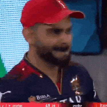 a man wearing a red hat and a blue shirt with the word birla on it is making a funny face .