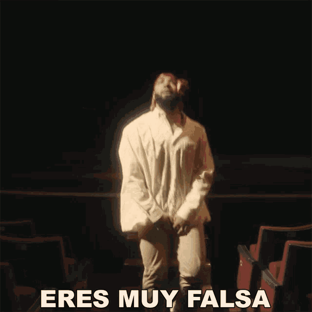 a man in a white shirt is dancing in an auditorium with the words eres muy falsa below him