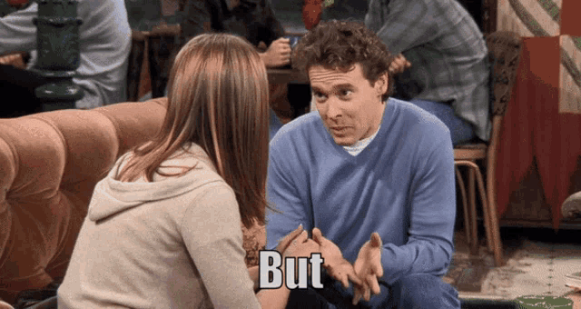 a man in a blue sweater is talking to a woman in a beige sweater and the words but are on the bottom