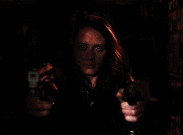 a woman in a leather jacket is pointing two guns