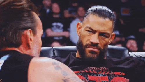 a man with a beard is sitting next to another man in a boxing ring .