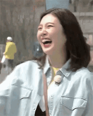 a woman in a denim jacket is laughing with her mouth wide open .