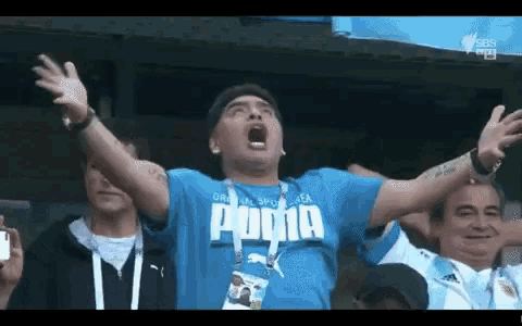 a man wearing a blue puma shirt is screaming with his arms outstretched .