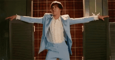 a man in a blue suit and white shirt is dancing in a room with his arms outstretched .