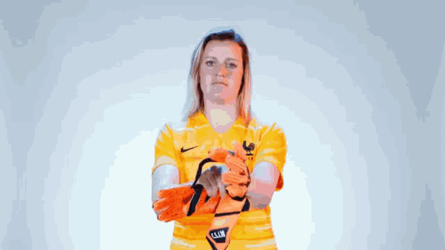 a woman wearing a yellow shirt and orange gloves holds her arms crossed