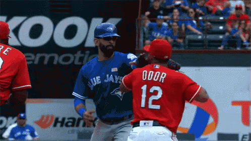 a baseball player in a blue jays jersey talks to another player in a red jersey