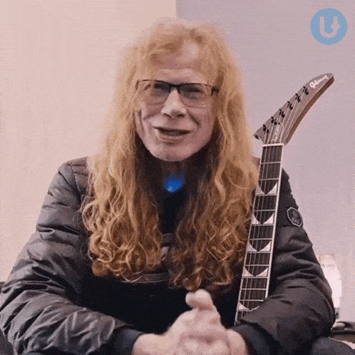 a man with long red hair and glasses holds a gibson guitar
