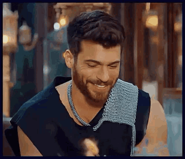 a man with a beard wearing a black tank top and a silver chain around his neck is smiling .