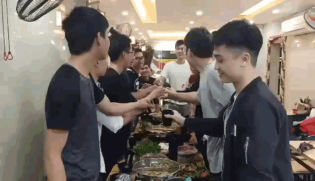 a group of young men are standing around a table in a restaurant toasting each other .