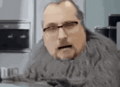 a man with glasses and a beard is wearing a sweater and a scarf around his neck .