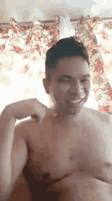 a shirtless man is smiling and flexing his muscles in front of a curtain .