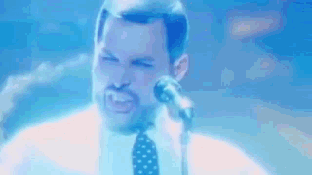 a man in a white shirt and tie is singing into a microphone on a stage .