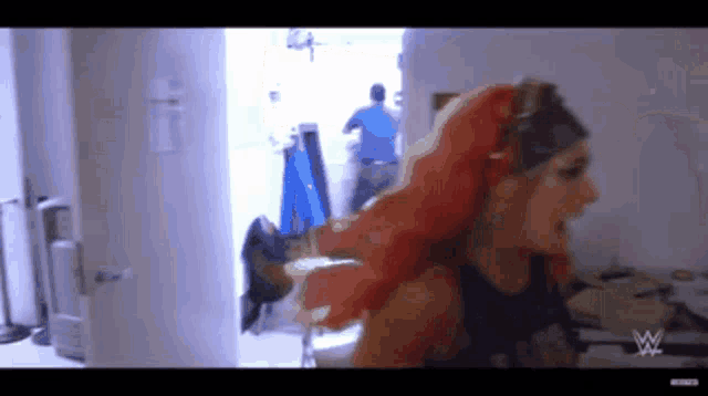 a woman with red hair is standing in a room with a wwe logo on the wall