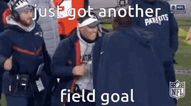 a man in a patriots jacket is talking to another man on a football field