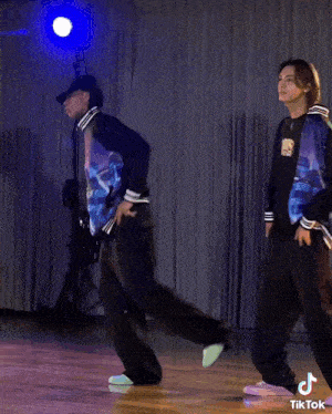 a couple of men are dancing in a room with a tiktok logo on the bottom right corner .