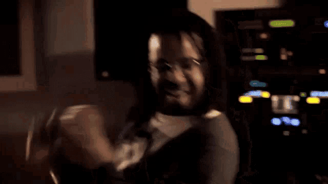 a man with long hair and glasses is standing in a dark room .