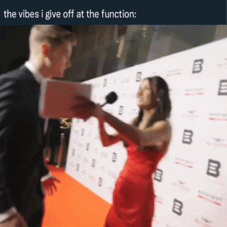 a woman in a red dress is talking into a microphone while a man in a suit looks on