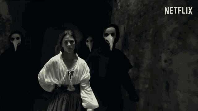 a woman is standing in front of a group of people wearing masks with long beaks .