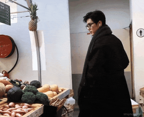 a man standing in front of a fruit stand with a pineapple hanging from the ceiling