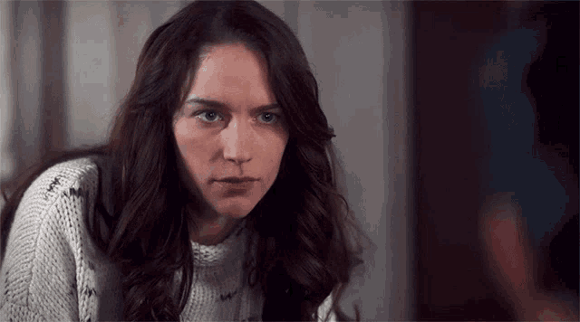 a woman in a white sweater looks at the camera with a serious look on her face