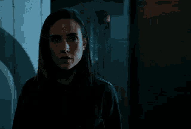 a woman with long dark hair is standing in a dark room looking at the camera .