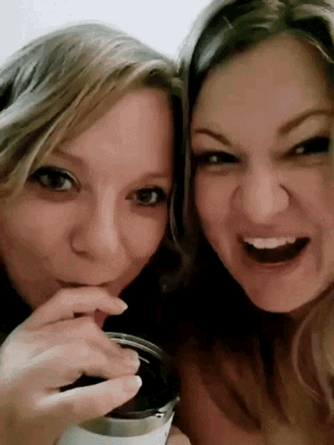 two women are making funny faces while drinking from a cup