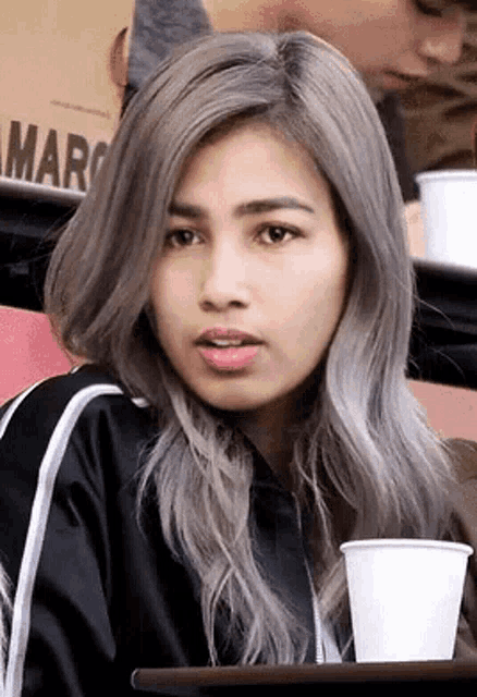 a woman with gray hair is sitting at a table with a cup of coffee in her hand .