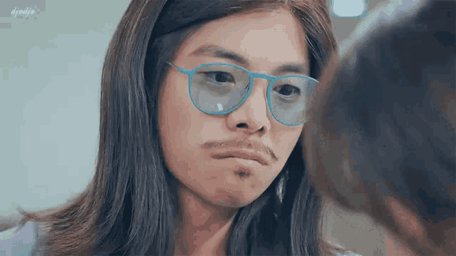 a man with long hair and glasses is looking at another man with a mustache .