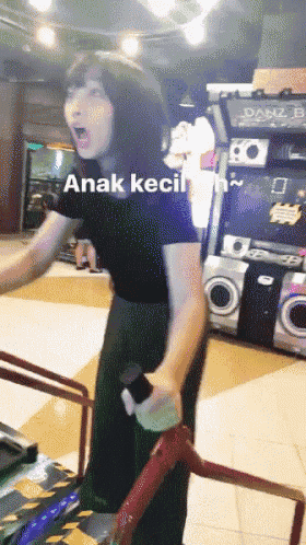 a woman in a black shirt is playing an arcade game with the words anak kecil written on the bottom