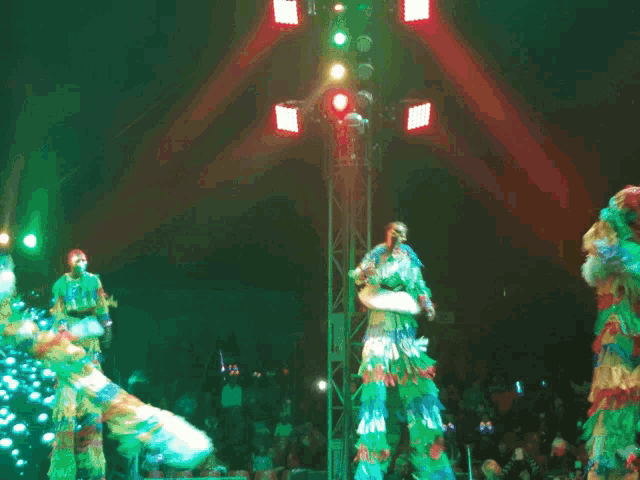 a group of people on stilts are dancing in front of a crowd of people