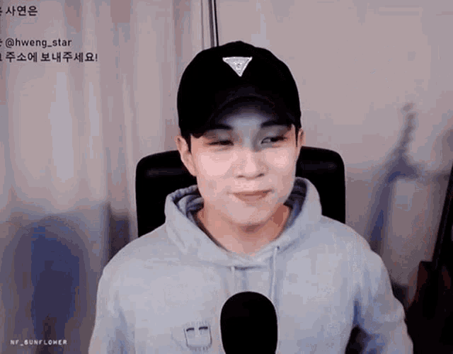 a man wearing a black hat and a blue hoodie is sitting in front of a microphone .