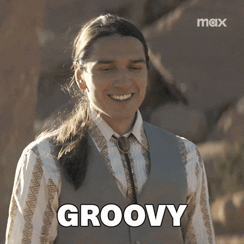 a man with long hair is smiling and the word groovy is on the screen