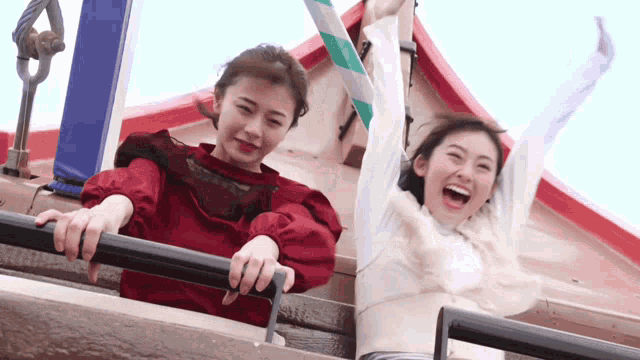 two women are riding a roller coaster with their arms up in the air