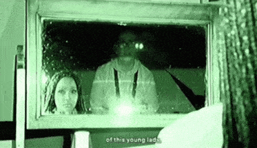 a woman is looking at her reflection in a mirror while a man is standing behind her .