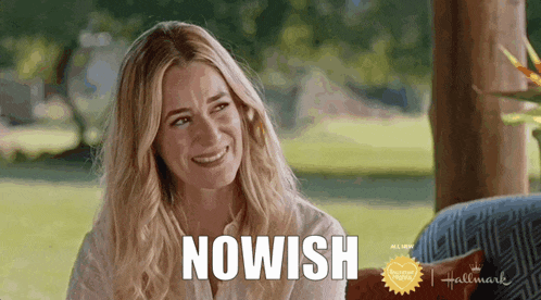 a woman is smiling while sitting on a couch and the word nowish is written on her face .