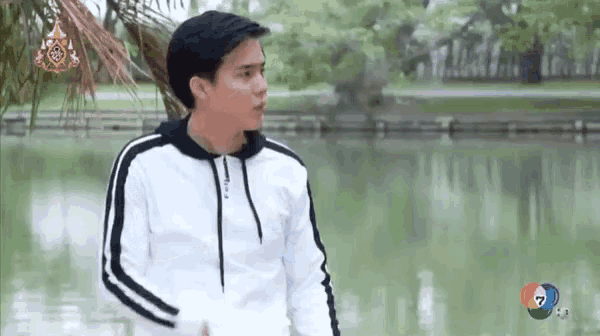 a young man in a white hoodie is standing in front of a lake .