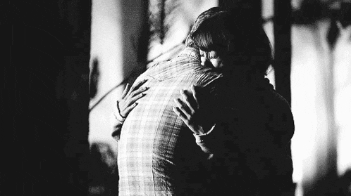 a black and white photo of a man and a woman hugging each other .