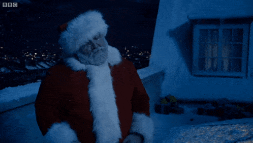 a man dressed as santa claus stands in front of a window with the bbc logo on the bottom
