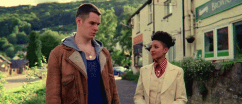 a man in a brown jacket and a woman in a white suit are standing in front of a building that says browns