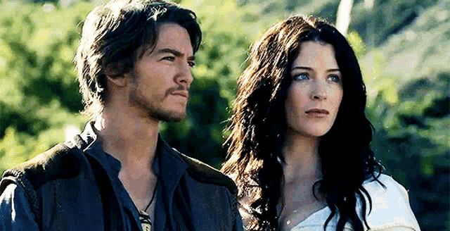 a man and a woman are standing next to each other in front of a forest .