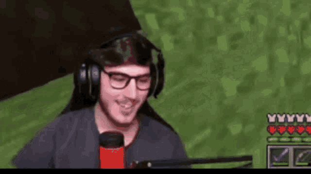 a man wearing headphones and glasses is smiling in front of a microphone while playing a video game .