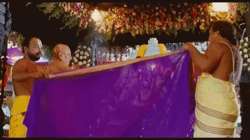 a group of men carrying a purple cloth with flowers hanging from the ceiling