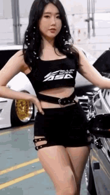 a woman in a black top and shorts is standing next to a car .