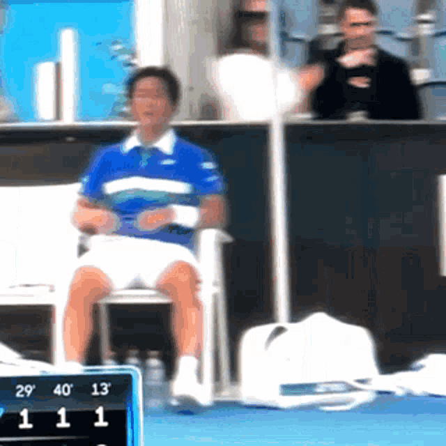 a man in a blue shirt sits in a chair in front of a scoreboard with the number 11