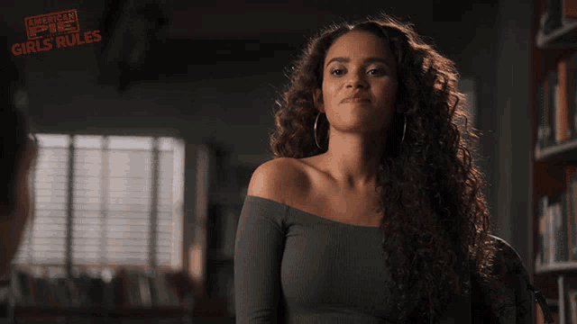a woman with curly hair says fine in front of a poster for american girls rules