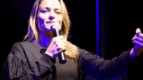 a woman singing into a microphone with fringe on her sleeves