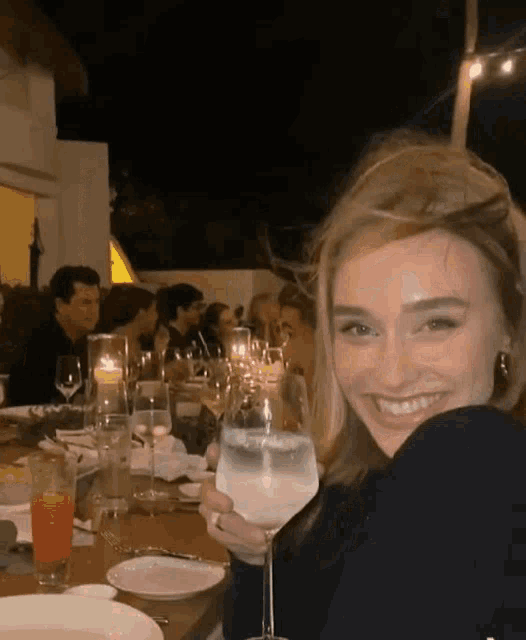 a woman is sitting at a table holding a glass of wine and smiling .