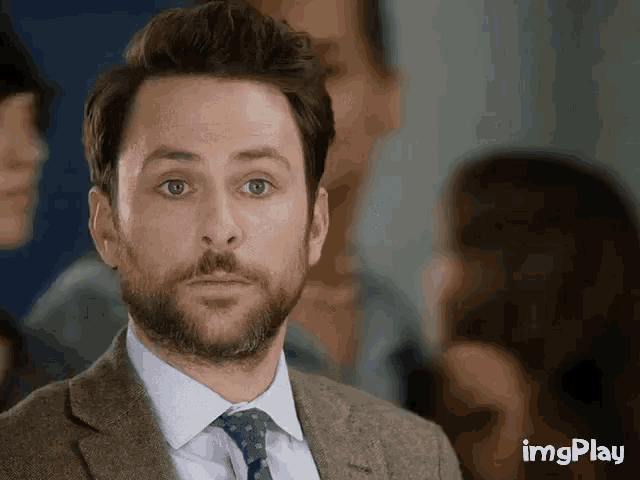 a man with a beard is wearing a suit and tie and looking at the camera .