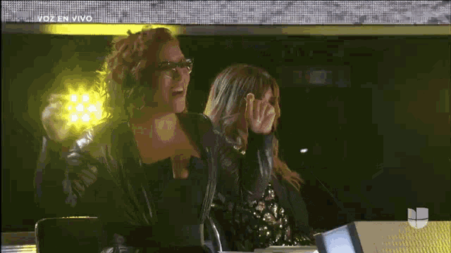 two women are sitting in front of a screen that says voz en vivo on it